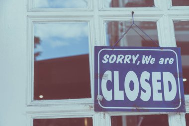 Kapalı olduğumuz için üzgün olduğumuzu belirten bir pano doğa yeşili arka planlı bir atölyenin kapısına asıldı.