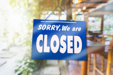 Kapalı olduğumuz için üzgün olduğumuzu belirten bir pano doğa yeşili arka planlı bir atölyenin kapısına asıldı.