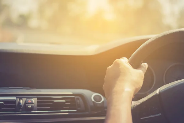 Hand of man on steering wheel drive a car with background.