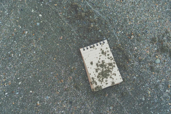 Pequeño cuaderno blanco sobre arena en la hermosa playa textura del mar . — Foto de Stock