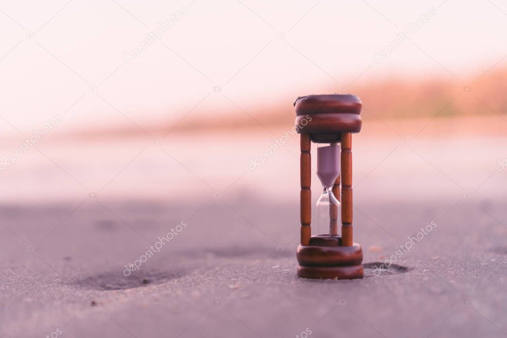 Small hourglass show time is flowing on sand at beautiful beach.