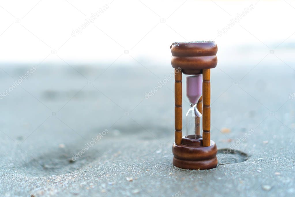 Small hourglass show time is flowing on sand at beautiful beach.