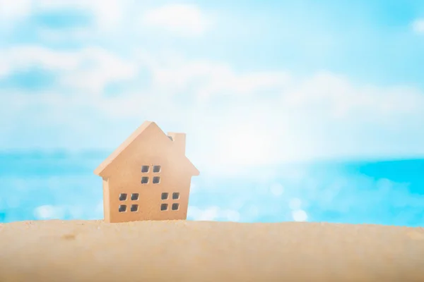 Cerrado pequeños modelos de casa en la arena con la luz del sol y la playa . — Foto de Stock