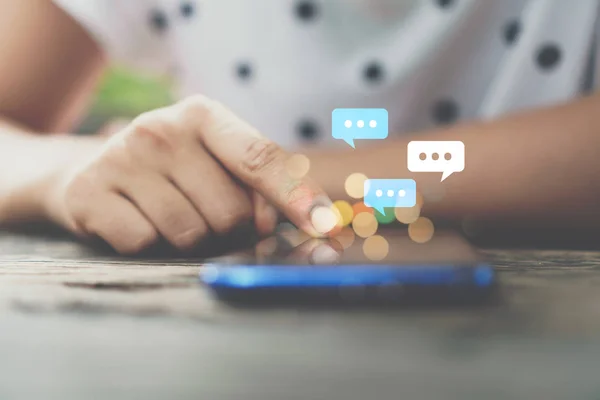 Mujer mano usando el teléfono inteligente con el icono de chat en el fondo de la cafetería . — Foto de Stock