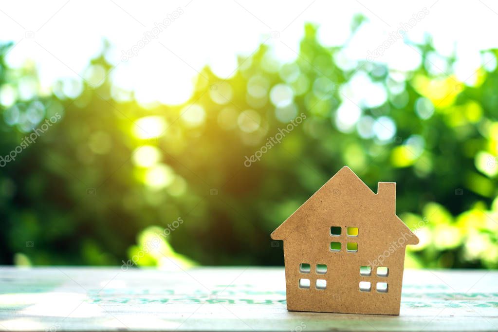 Closed up tiny home model on floor or wood board with sunlight green bokeh background. House property for living or investment concept.
