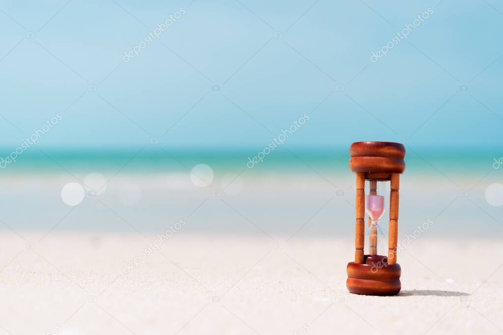 Small hourglass show time is flowing on sand beach texture background.