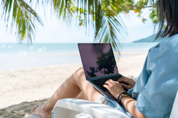 Plaj arka planında tatil malzemelerinde çalışmak için dizüstü bilgisayar ve akıllı telefon kullanan bir kadın. İş, finans, ticaret hisseleri ve sosyal ağ kavramı.
