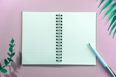 Çerçeve arkaplan olarak tropikal yaprak içeren boş alan beyaz defter ve kalemin üst görünümü.