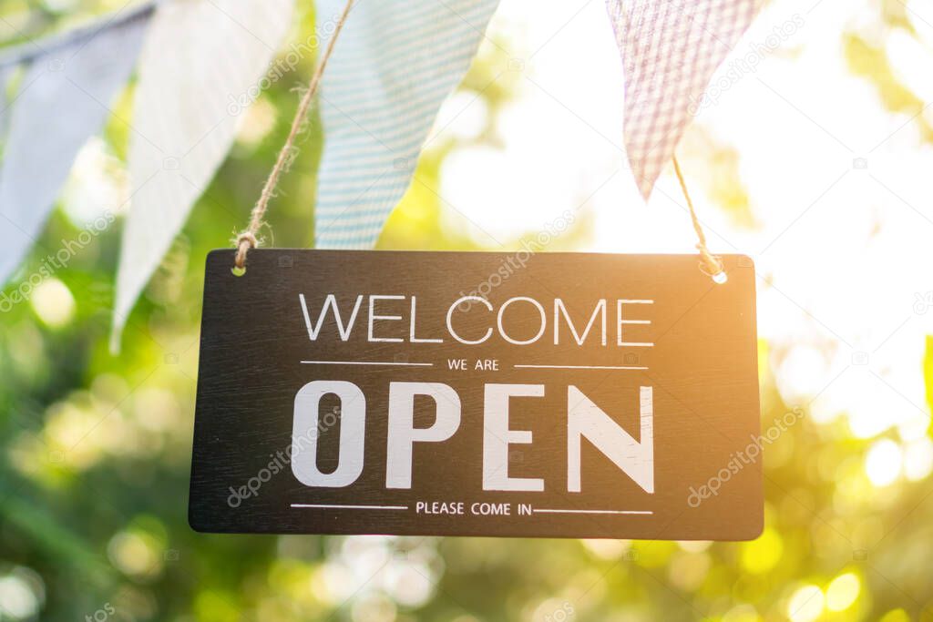 A business sign that says open on cafe or restaurant hang on tree at entrance of shop with sun light bokeh background