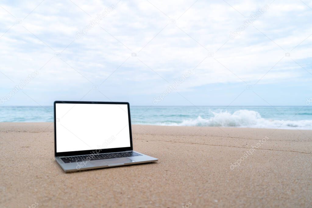 Laptop on sand at summer beach in background with white screen.