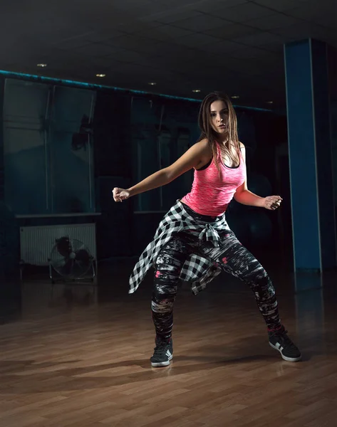 Young attractive brunette woman doing zumba dance workout alone in gym. Toned image.