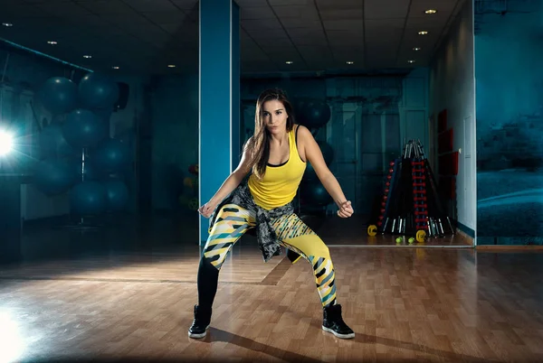 Young attractive brunette woman doing zumba dance workout alone in gym. Toned image.