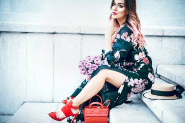 Çiçekli taş merdivenle oturan çekici genç bayan. Tonlu görüntü.