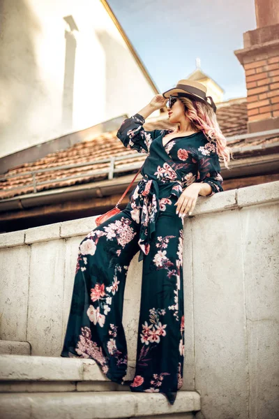 Beautiful sensual fashion woman with purse and hat posing on white stone stairs in Sarajevo old town. Toned image.