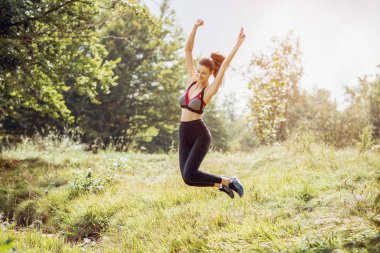 Yüksek atlama genç mutlu spor kadın çayır üzerinde açık. Tonlu görüntü.