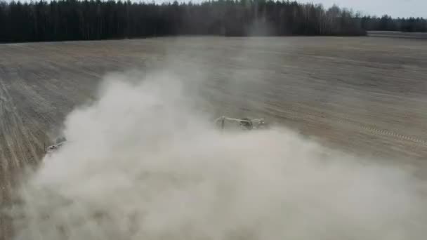 Trator que processa terras agrícolas empoeiradas e de baixo rendimento usando uma unidade de semeadura de lavoura. O drone segue a máquina agrícola. Conceito de agronegócio — Vídeo de Stock