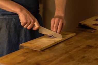 Chef cutting green onions on wooden board in dim light.