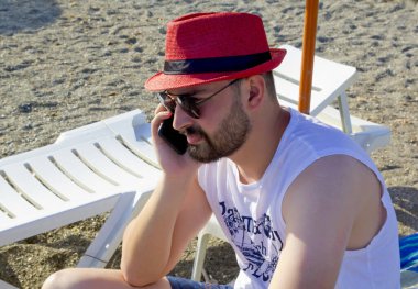 Kumsaldaki kırmızı şapkalı yakışıklı genç.