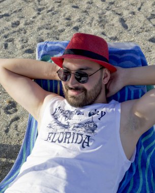 Güneş gözlüklü yakışıklı genç adam sahilde dinleniyor.