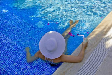 Havuzda dinlenen beyaz şapkalı genç bir kadın.