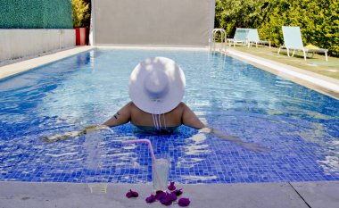 Havuzda dinlenen beyaz şapkalı genç bir kadın.