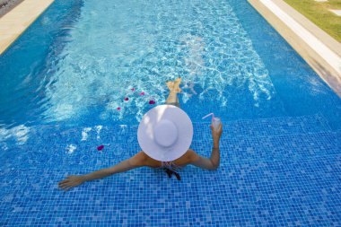 Havuzda dinlenen beyaz şapkalı genç bir kadın.