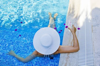 Havuzda dinlenen beyaz şapkalı genç bir kadın.