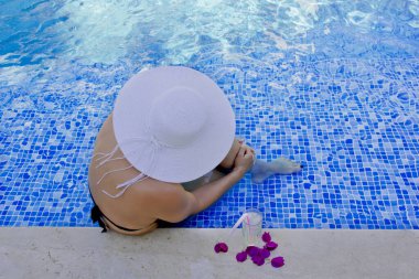 Havuzda dinlenen beyaz şapkalı genç bir kadın.