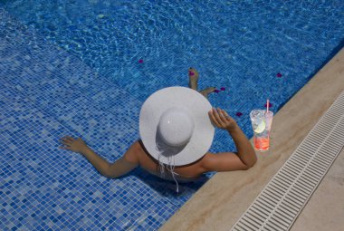 Havuzda dinlenen beyaz şapkalı genç bir kadın.