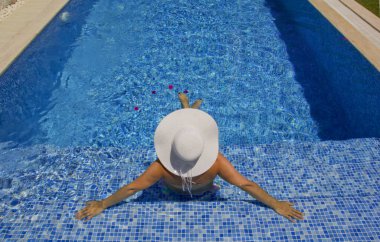 Havuzda dinlenen beyaz şapkalı genç bir kadın.