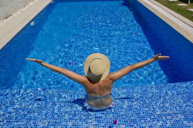 Havuzda dinlenen beyaz şapkalı genç bir kadın.