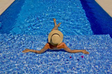 Havuzda dinlenen beyaz şapkalı genç bir kadın.