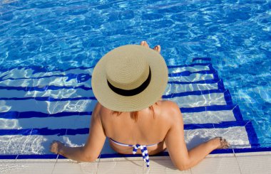 Havuzda dinlenen beyaz şapkalı genç bir kadın.
