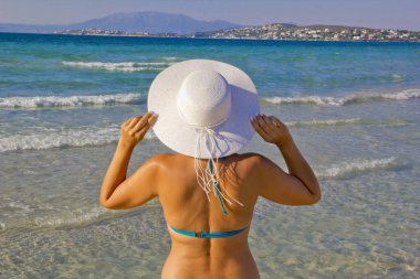  Bikinili genç bir kadın plajda beyaz bir şapka