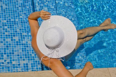 Havuzda dinlenen beyaz şapkalı genç bir kadın.
