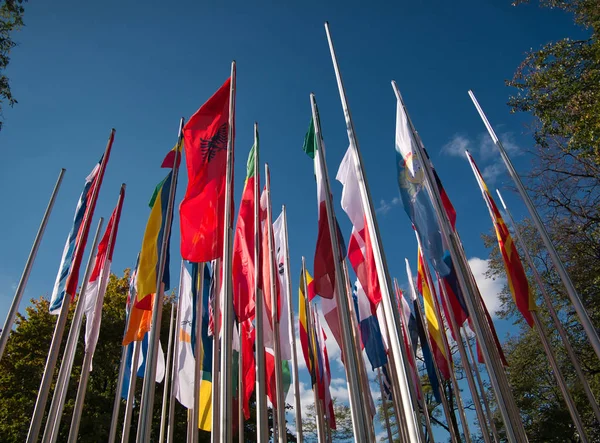 Several flagpoles with different flags in the wind before blue sky as background