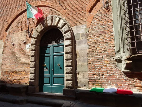 Three cushions in green, white and red like the Italian flag next to a green wooden door