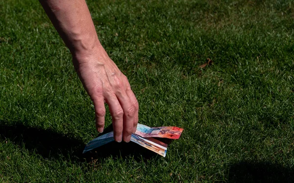 hand picking up money from the ground. swiss currency. grass ground swiss francs
