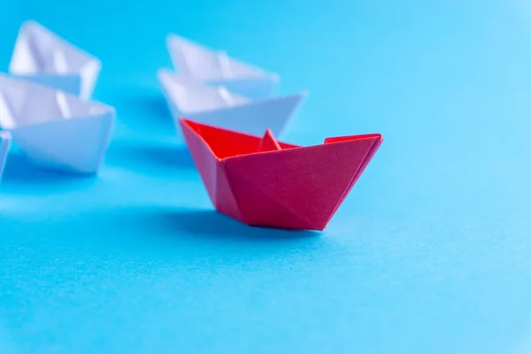 White and red paper boat or ship in one direction on blue background. Business for innovative solution concept with selective focus