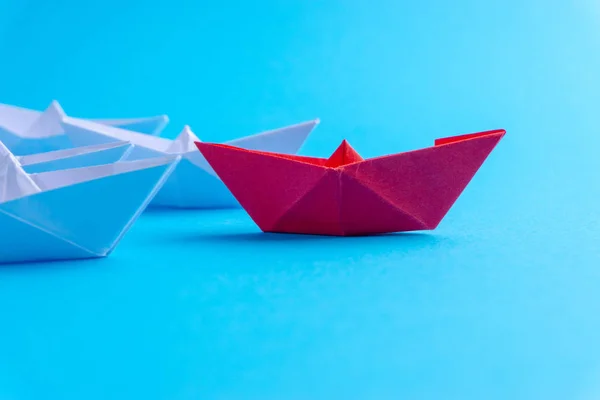 White and red paper boat or ship in one direction on blue background. Business for innovative solution concept with selective focus