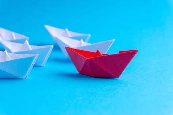 White and red paper boat or ship in one direction on blue background. Business for innovative solution concept with selective focus