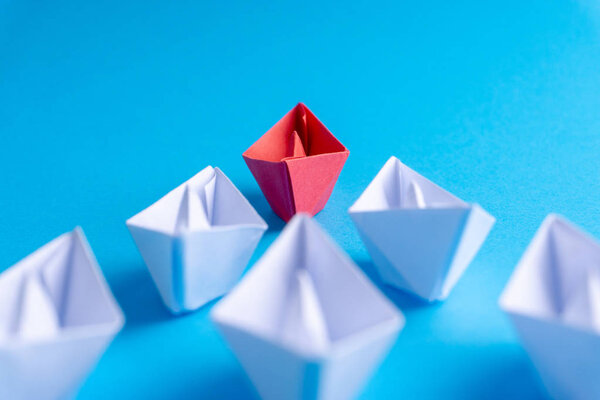 White and red paper boat or ship in one direction on blue background. Business for innovative solution concept with selective focus