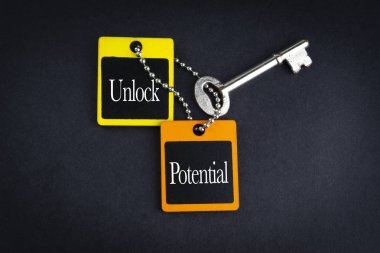 UNLOCK POTENTIAL inscription written on wooden tag and key on black background with selective focus and crop fragment. Business and education concept clipart