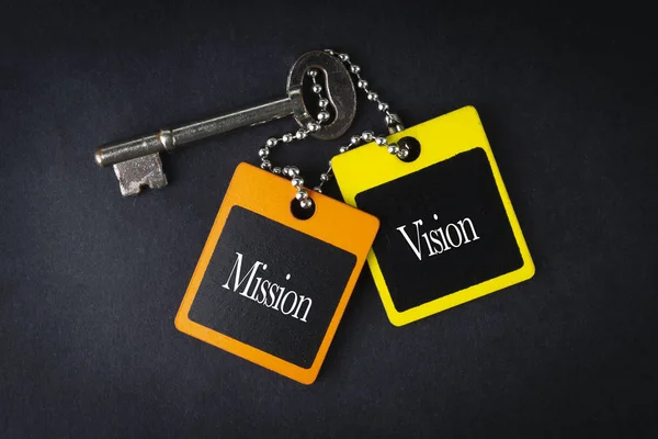 MISSION VISION inscription written on wooden tag and key on black background with selective focus and crop fragment. Business and education concept