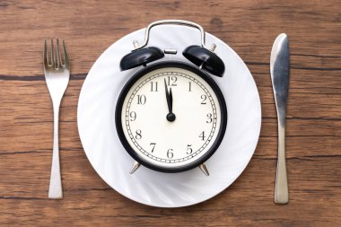 Alarm clock with fork and knife on the table. Time to eat, Breakfast, Lunch time and dinner concept. clipart