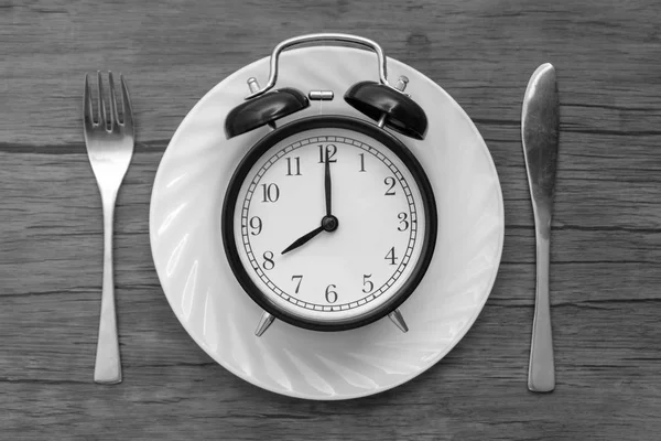 テーブルの上のナイフとフォークの目覚まし時計 時間を食べる 昼食の時間と夕食の概念 黒と白のコンセプト — ストック写真