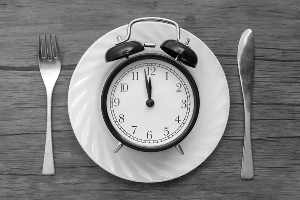 テーブルの上のナイフとフォークの目覚まし時計 時間を食べる 昼食の時間と夕食の概念 黒と白のコンセプト — ストック写真