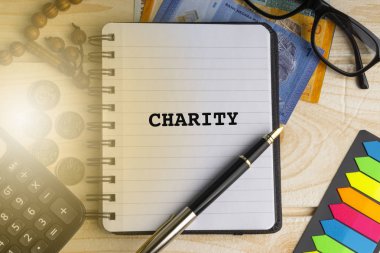 Sadaka kitabe üzerinde kitap yazılmış hesap makinesi, tespih, madeni para, banknot, kitap, gözlük ve ahşap arka plan üzerinde kalem. İş, sigorta ve İslam kavramı