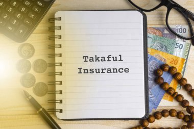 Takaful sigorta (İslam sigorta) kitabe üzerinde kitap yazılmış hesap makinesi, tespih, madeni para, banknot, kitap, gözlük ve ahşap arka plan üzerinde kalem. İş, sigorta ve İslam kavramı