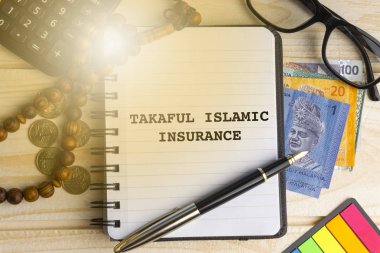 Takaful İslam sigorta kitabe üzerinde kitap yazılmış hesap makinesi, tespih, madeni para, banknot, kitap, gözlük ve ahşap arka plan üzerinde kalem. İş, sigorta ve İslam kavramı